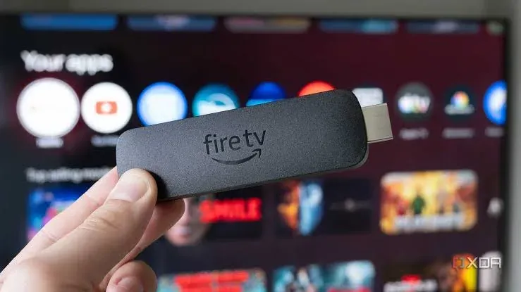 Hand holding an Amazon Fire TV stick in front of a TV app screen